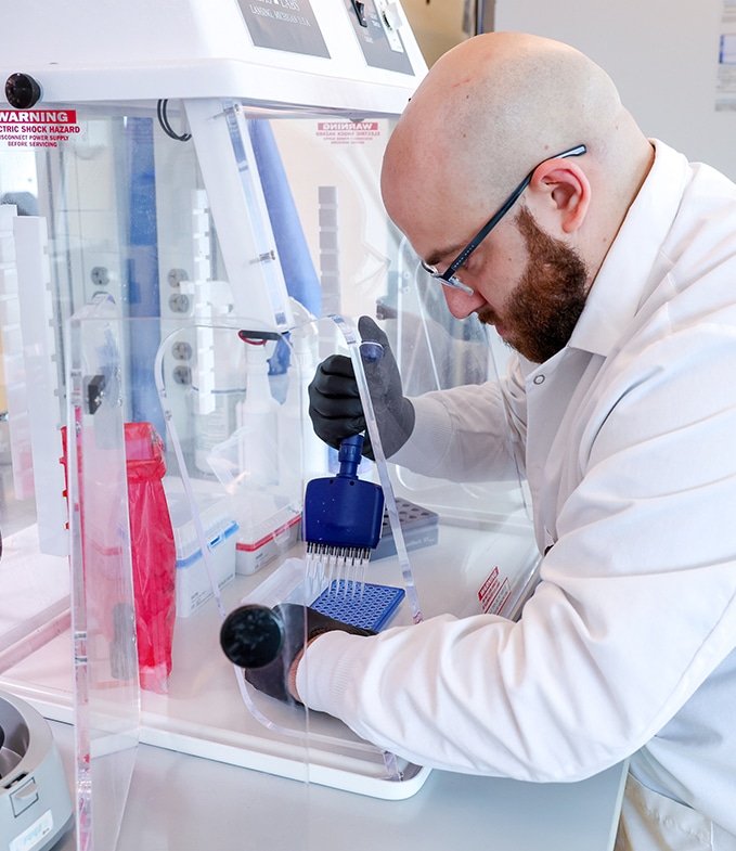 A scientist fills multiple vials at once with a manual tool inside a fume hood