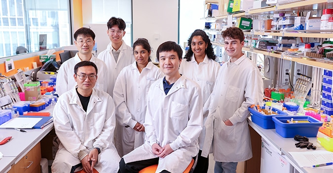 A group of seven scientists in lab coats pose as a group in a lab setting