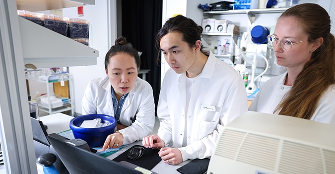 Three scientists in lab coats have a discussion in a lab