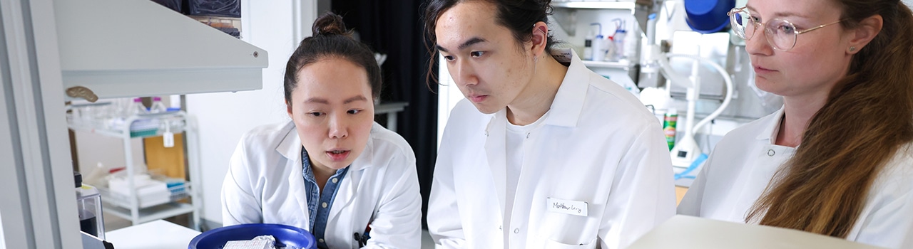 Three scientists in lab coats have a discussion in a lab