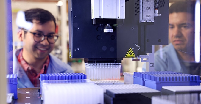 Two scientists watch a machine fill a tray of vials