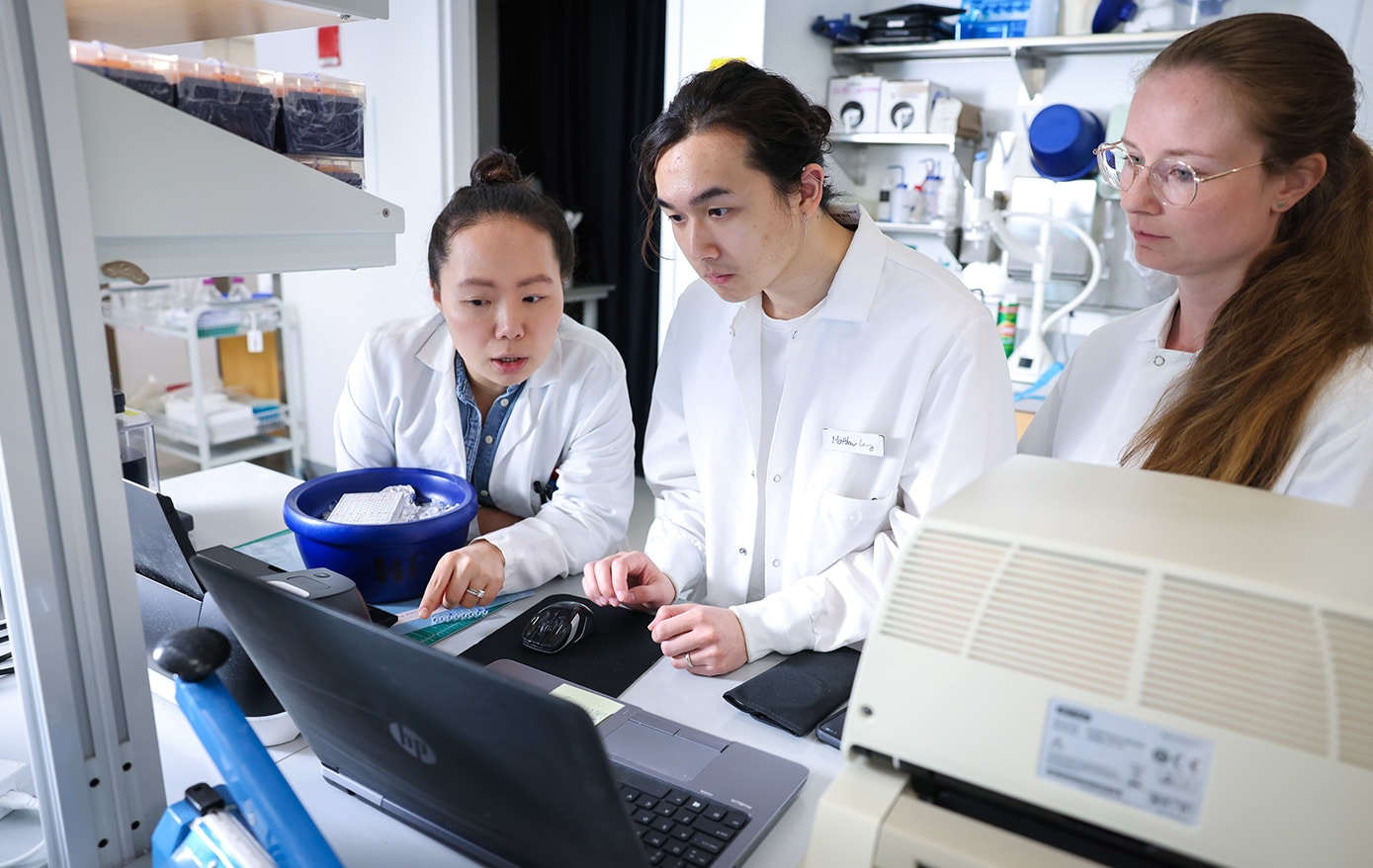 Three scientists in lab coats have a discussion in a lab