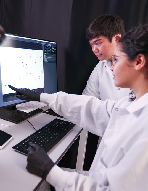 One scientist points out a cell on a micrograph while another scientist looks on